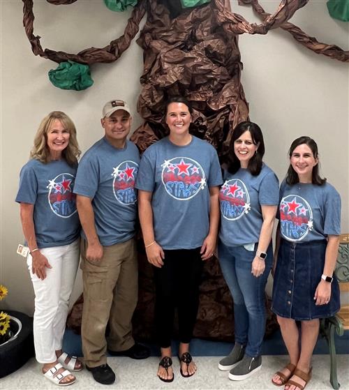 Mrs. Pickles, Coach Perez, Coach Keating, Ilene Baumel, and Courtney Walker smiling in front of a paper tree.